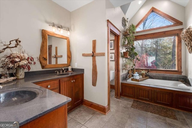 bathroom featuring vanity, toilet, a garden tub, lofted ceiling, and baseboards