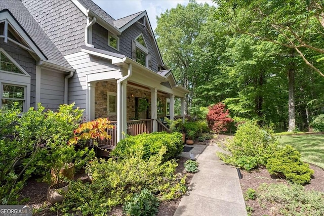 view of home's exterior with stone siding, a porch, and roof with shingles