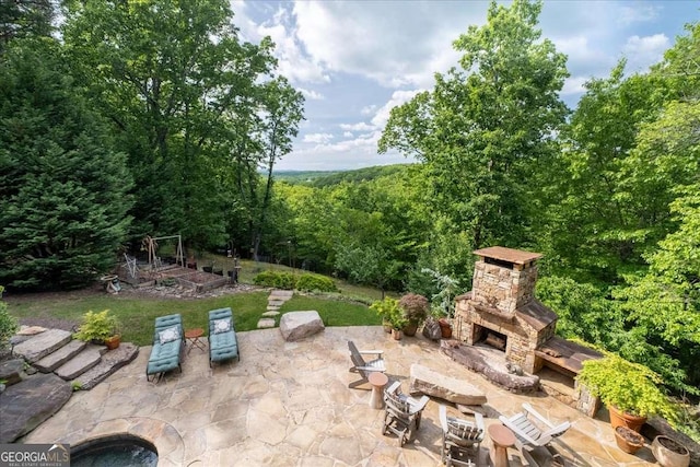 view of patio / terrace featuring an outdoor stone fireplace, a wooded view, and a vegetable garden