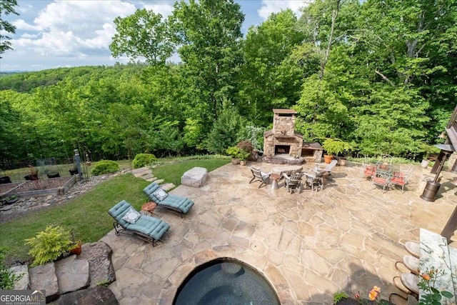 view of patio with an outdoor stone fireplace, a wooded view, and a vegetable garden