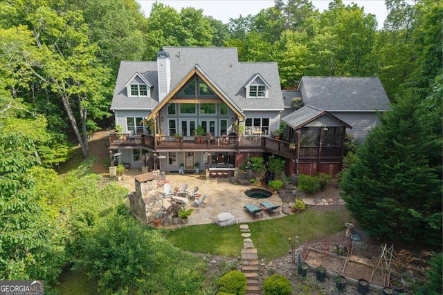 rear view of property featuring a patio, a deck, a sunroom, a chimney, and an outdoor fire pit