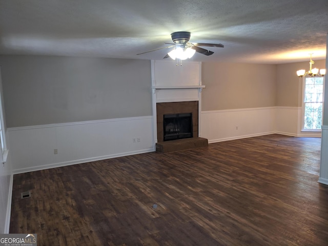 135 Beverly Park Ct, Newnan, GA 30263 - unfurnished living room featuring a wainscoted wall, dark wood-style flooring, a chandelier, a fireplace with raised hearth, and a textured ceiling
