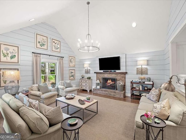 living room with a chandelier, wood finished floors, a brick fireplace, wooden walls, and high vaulted ceiling