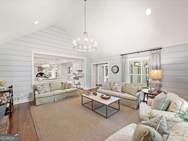 living room featuring a chandelier, wooden walls, dark wood-style floors, plenty of natural light, and high vaulted ceiling
