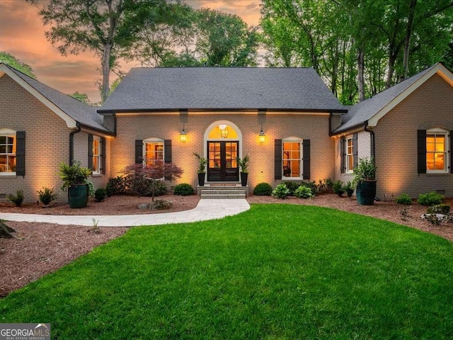 view of front of house with french doors, a front yard, brick siding, and a shingled roof