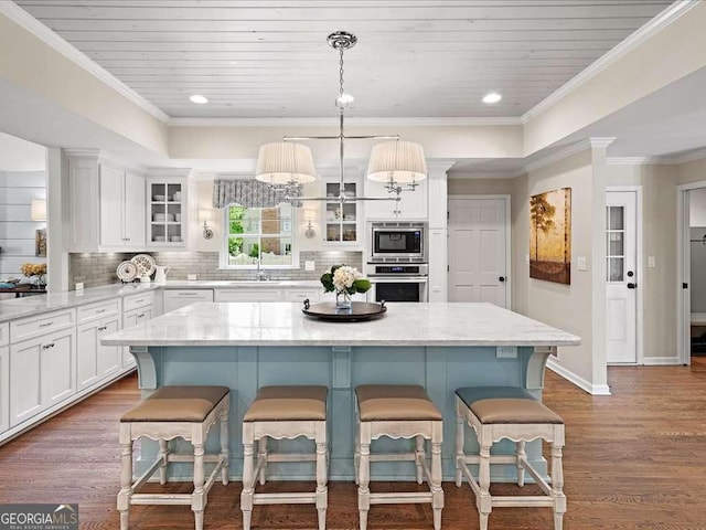kitchen with appliances with stainless steel finishes, white cabinets, backsplash, glass insert cabinets, and a kitchen island