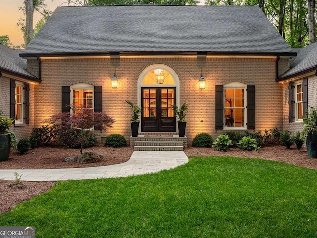 view of front facade featuring entry steps, brick siding, french doors, a front yard, and roof with shingles