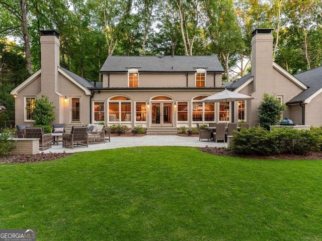 rear view of property with french doors, a chimney, a patio, a yard, and brick siding