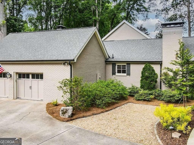 view of home's exterior with a garage, driveway, brick siding, and a chimney