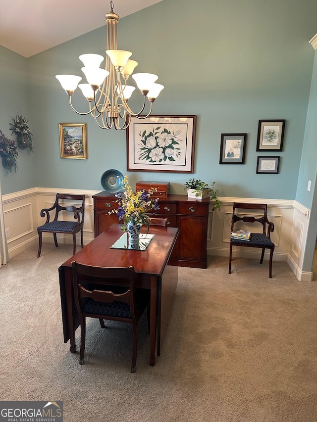 dining room featuring light colored carpet, a chandelier, lofted ceiling, wainscoting, and a decorative wall