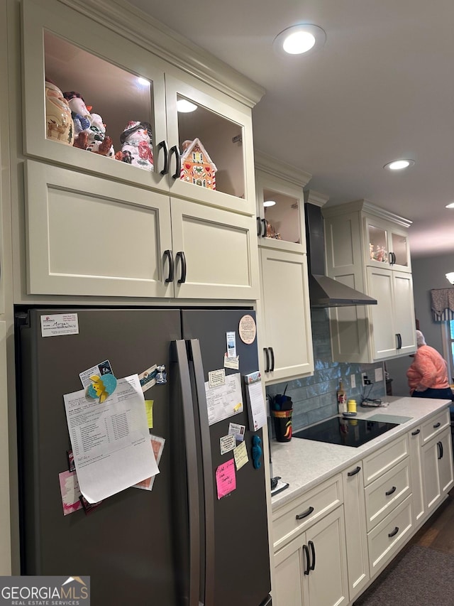 kitchen with freestanding refrigerator, black electric stovetop, wall chimney range hood, white cabinets, and backsplash