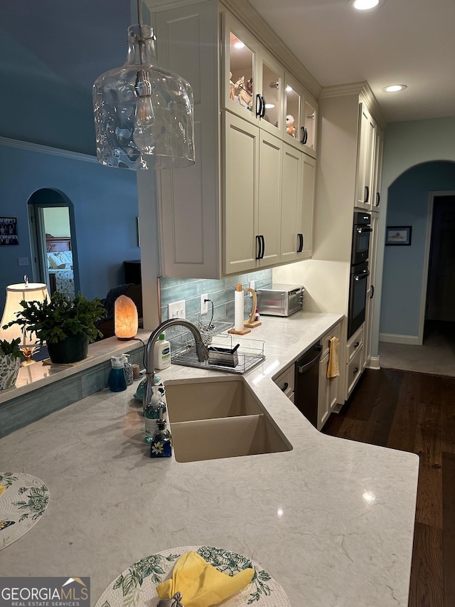 kitchen with arched walkways, a sink, glass insert cabinets, light stone countertops, and dark wood-type flooring