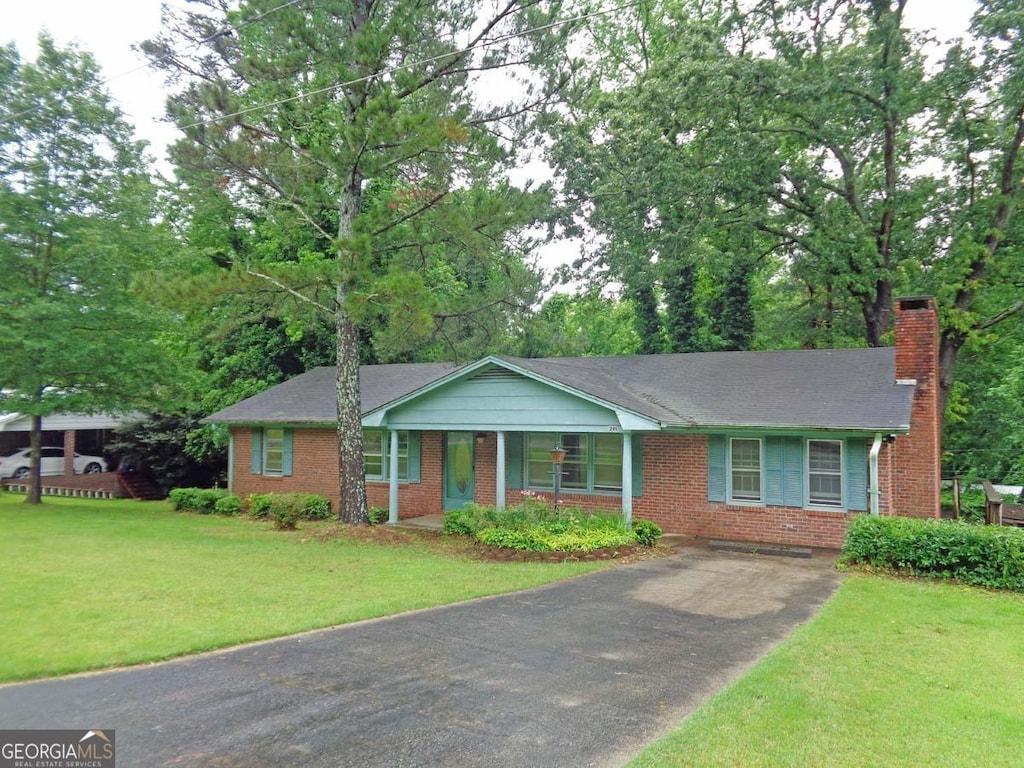 ranch-style house featuring driveway, a chimney, brick siding, and a front yard