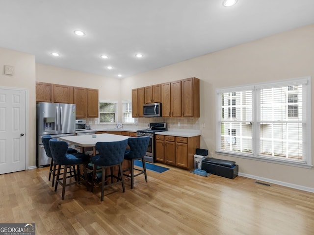 361 Brackin Trce, Grayson, GA 30017 - kitchen with appliances with stainless steel finishes, brown cabinets, a breakfast bar, light wood-type flooring, and decorative backsplash