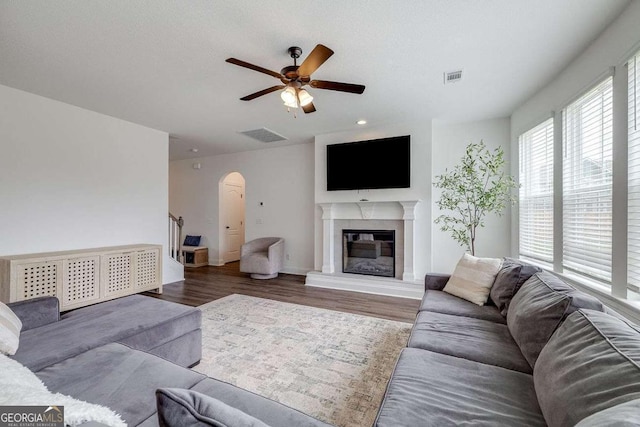 living area featuring ceiling fan, arched walkways, wood finished floors, a glass covered fireplace, and recessed lighting