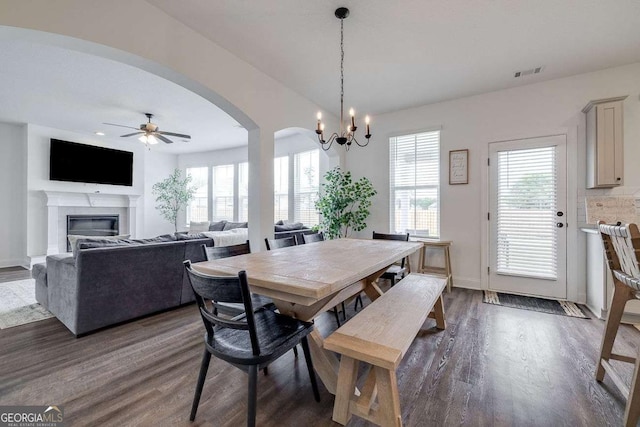 dining room with arched walkways, dark wood-style flooring, ceiling fan, a glass covered fireplace, and baseboards