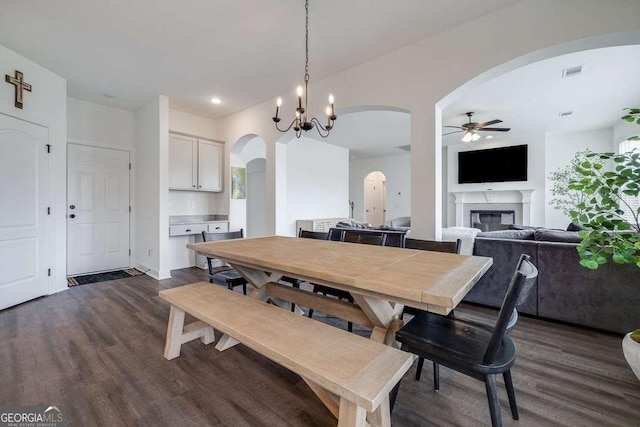 dining area with arched walkways, dark wood finished floors, a ceiling fan, a glass covered fireplace, and recessed lighting