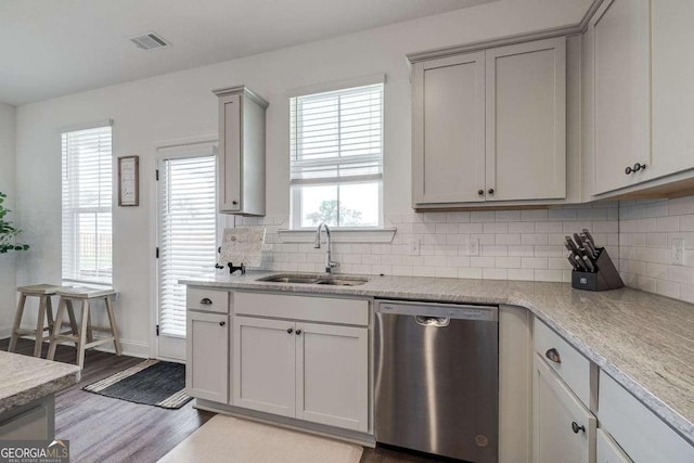 kitchen featuring stainless steel dishwasher, a sink, backsplash, wood finished floors, and light countertops