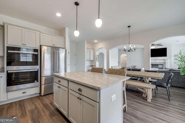 kitchen with stainless steel appliances, arched walkways, open floor plan, dark wood finished floors, and a glass covered fireplace