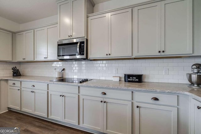 kitchen featuring stainless steel microwave, black electric stovetop, dark wood finished floors, and tasteful backsplash