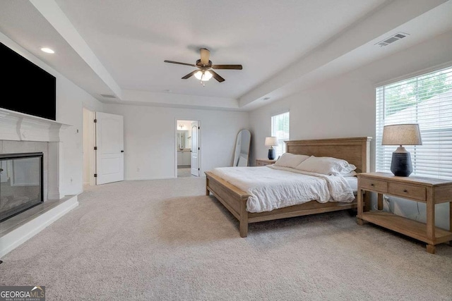 bedroom with carpet floors, a tray ceiling, a glass covered fireplace, baseboards, and ceiling fan