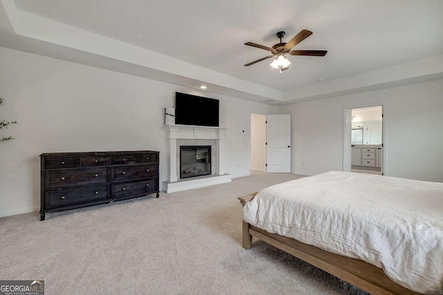 bedroom featuring a tray ceiling, carpet, a glass covered fireplace, baseboards, and recessed lighting