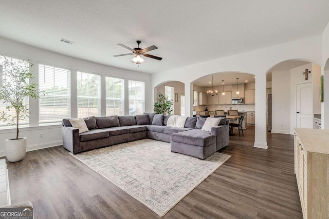 living area with a ceiling fan, dark wood-style flooring, baseboards, and arched walkways