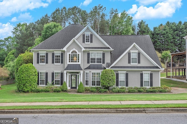 colonial-style house with stucco siding, a standing seam roof, a front lawn, roof with shingles, and metal roof