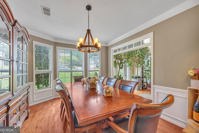 dining area featuring a chandelier, crown molding, light wood-type flooring, a wainscoted wall, and a decorative wall
