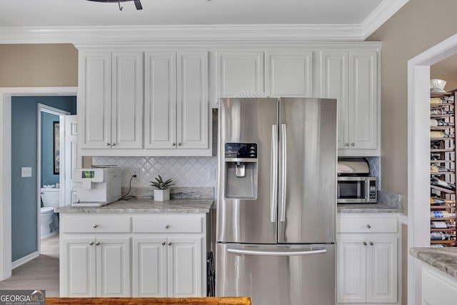 kitchen featuring stainless steel appliances, white cabinetry, decorative backsplash, crown molding, and light stone countertops