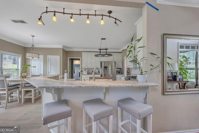 kitchen featuring stainless steel fridge, healthy amount of natural light, a breakfast bar, and crown molding