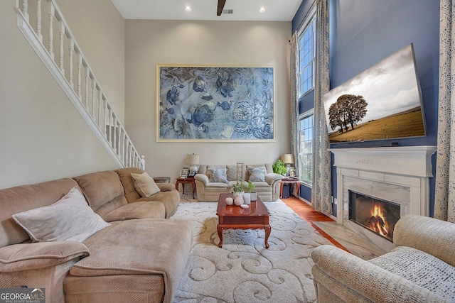 living room featuring wood finished floors, a premium fireplace, stairs, a high ceiling, and recessed lighting