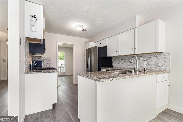 kitchen with stainless steel fridge with ice dispenser, a sink, wood finished floors, light stone countertops, and white cabinets