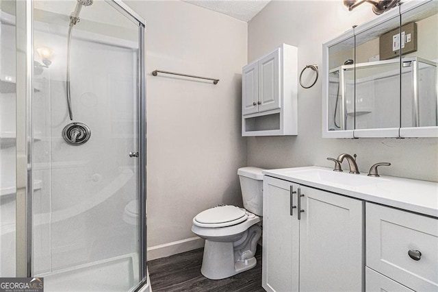 bathroom with wood finished floors, a shower stall, toilet, vanity, and baseboards