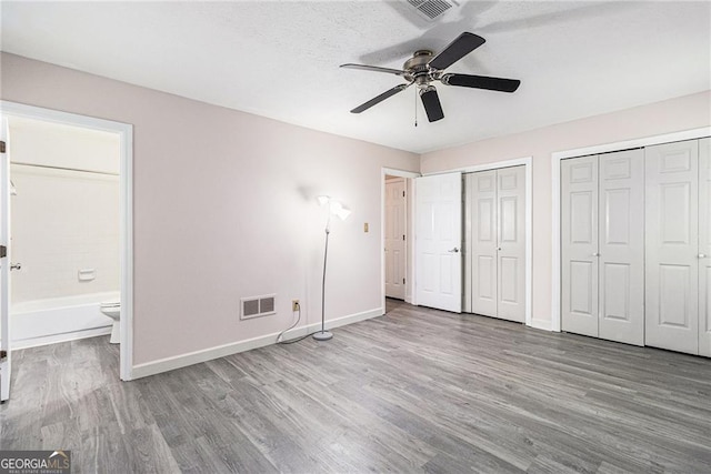 unfurnished bedroom with wood finished floors, baseboards, and multiple closets