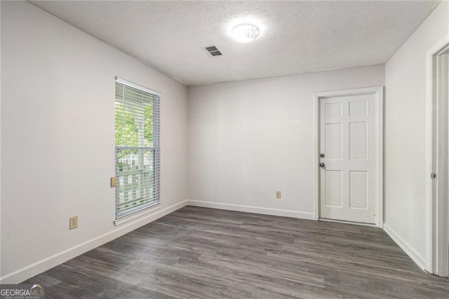empty room with a textured ceiling, dark wood-type flooring, and baseboards