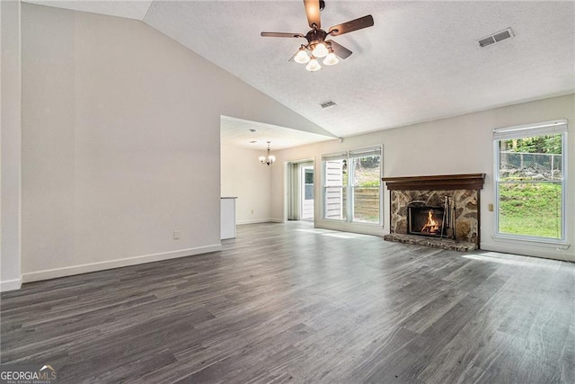 unfurnished living room with dark wood-type flooring, a stone fireplace, a chandelier, a ceiling fan, and a textured ceiling