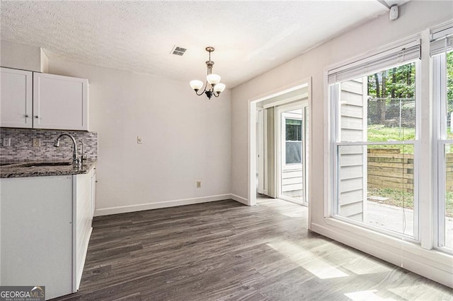 unfurnished dining area with a sink, a chandelier, dark wood finished floors, baseboards, and a textured ceiling