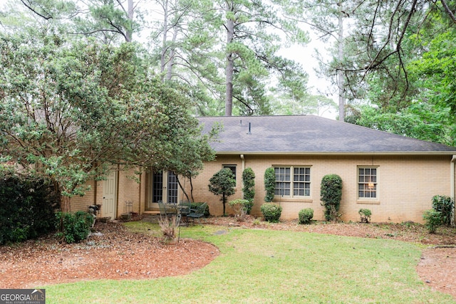 view of front of home featuring brick siding, roof with shingles, and a front yard