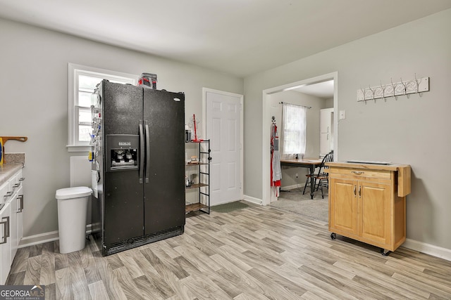 kitchen featuring black fridge, light wood finished floors, plenty of natural light, and baseboards