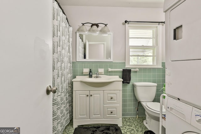 bathroom featuring stacked washing machine and dryer, tile walls, toilet, vanity, and a wainscoted wall