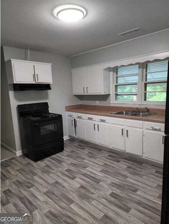 kitchen with black electric range oven, white cabinetry, wood finished floors, a sink, and under cabinet range hood