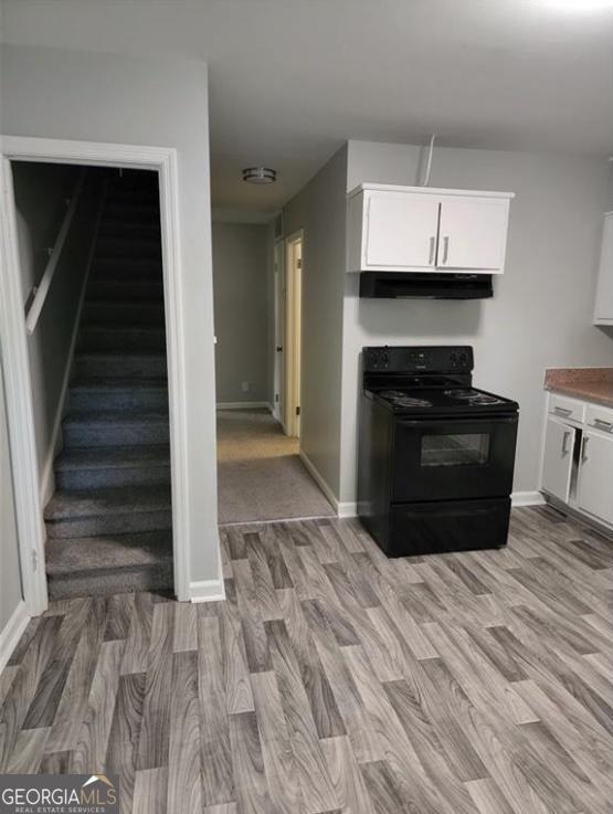 kitchen featuring black electric range, under cabinet range hood, light wood finished floors, white cabinetry, and baseboards