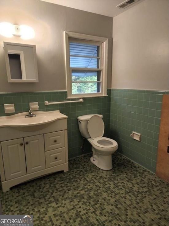 bathroom featuring a wainscoted wall, toilet, tile walls, and vanity