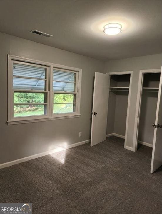 unfurnished bedroom featuring two closets, dark carpet, and multiple windows