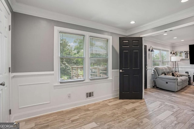 entrance foyer with light wood finished floors, a wainscoted wall, crown molding, and a decorative wall