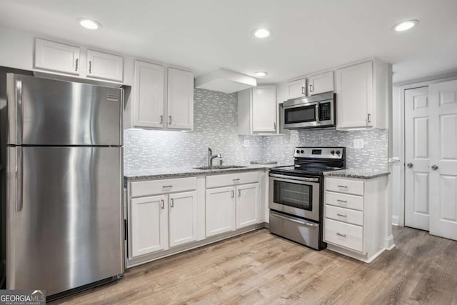kitchen featuring stainless steel appliances, a sink, white cabinets, light wood-style flooring, and light stone counters