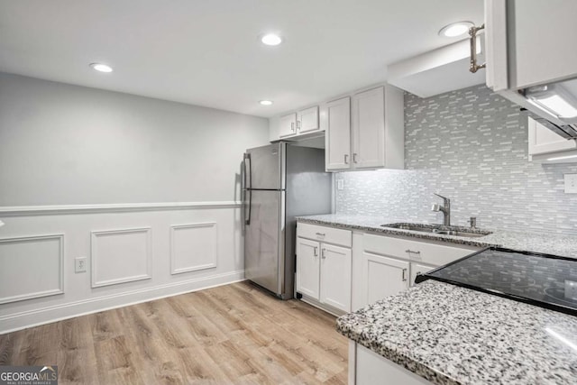 kitchen featuring a sink, freestanding refrigerator, light stone counters, white cabinets, and tasteful backsplash