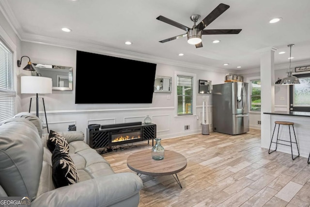 living area featuring ceiling fan, light wood-style flooring, recessed lighting, crown molding, and a glass covered fireplace
