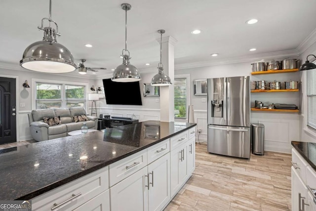 kitchen with stainless steel fridge, crown molding, white cabinets, open floor plan, and dark stone countertops